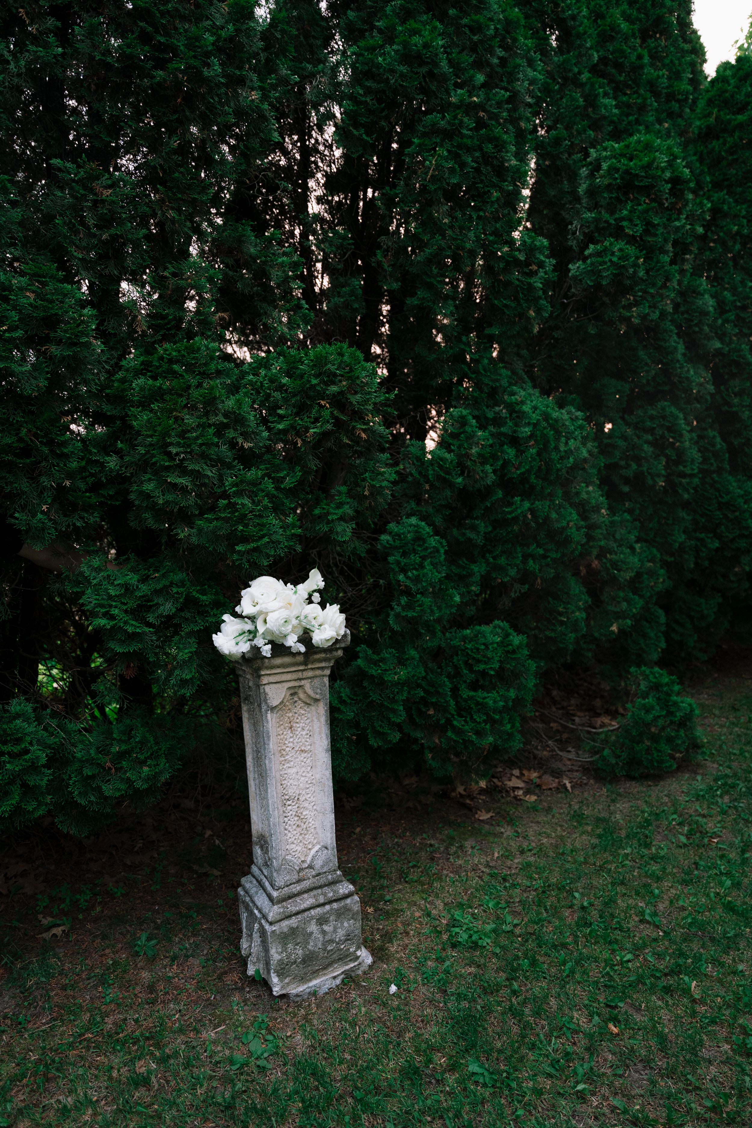 A weathered stone monument stands solemnly among green trees in a cemetery setting.
