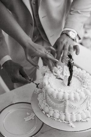 A sequence of black and white photos showing hands cutting into a traditional white wedding cake with decorative frosting.