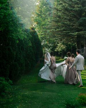 A group in formal attire poses dramatically on a lush green lawn surrounded by trees.
