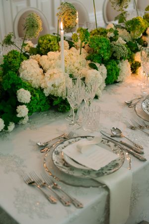 Elegant table setting with white and green floral centerpieces, crystal glassware, and fine china.
