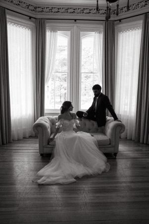 Black and white photo of couple sharing intimate moment on sofa by bay windows.