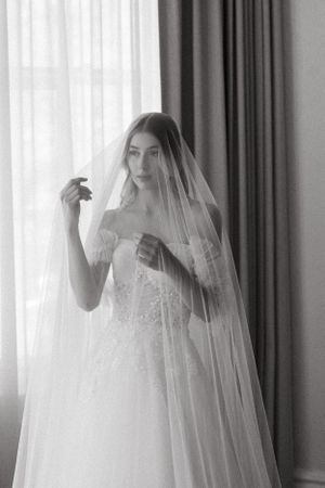 A black and white portrait of a bride wearing a delicate lace veil and strapless wedding gown.