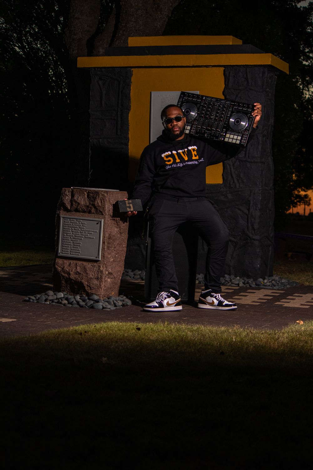 Person holding DJ controller at night against dark backdrop with yellow accents.