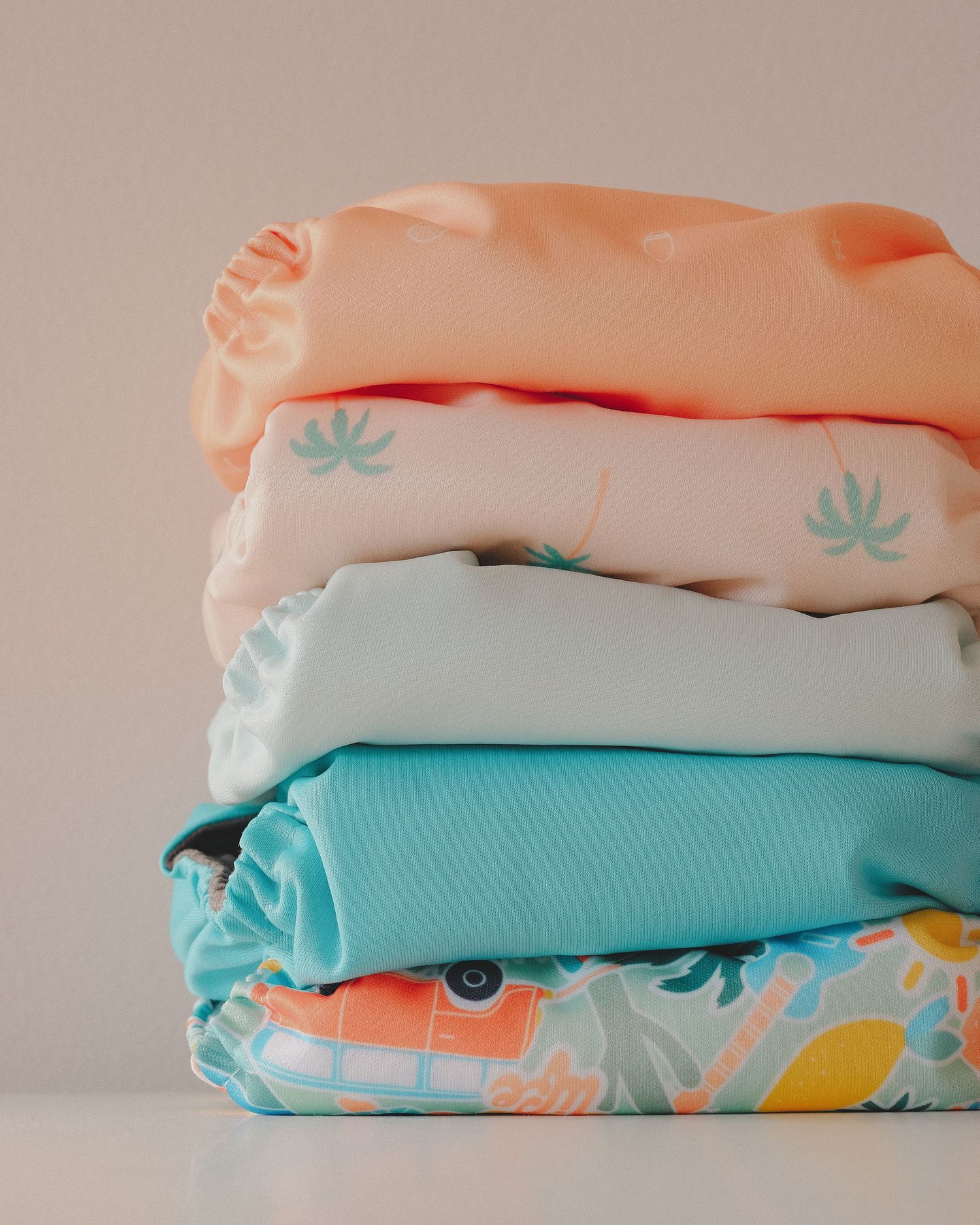 Neatly folded cloth diapers in soft pastel shades stacked on a neutral background.