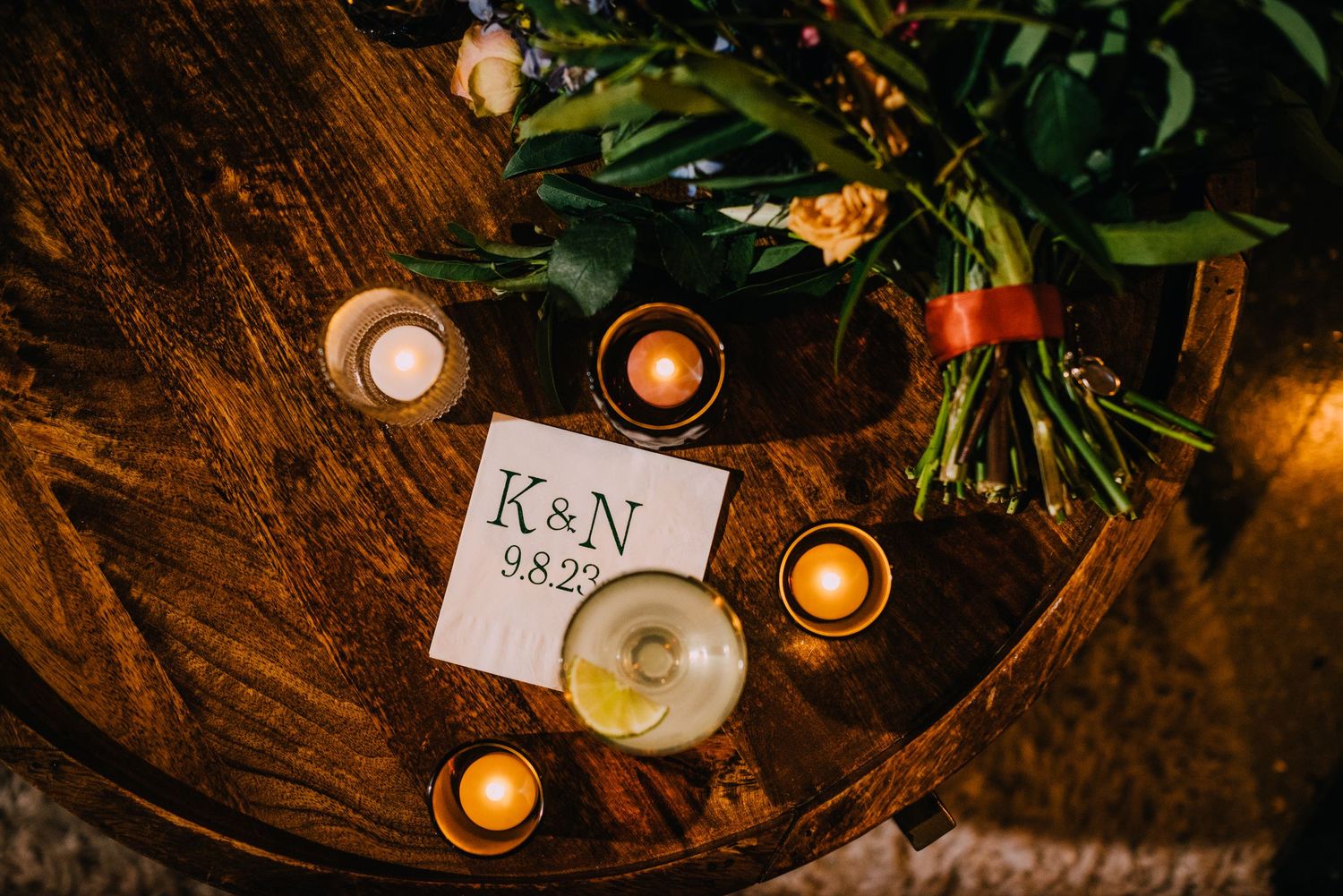 Candles glimmer on a dark wooden table set for a Krystyn and Nates wedding with modern napkins and stunning florals.