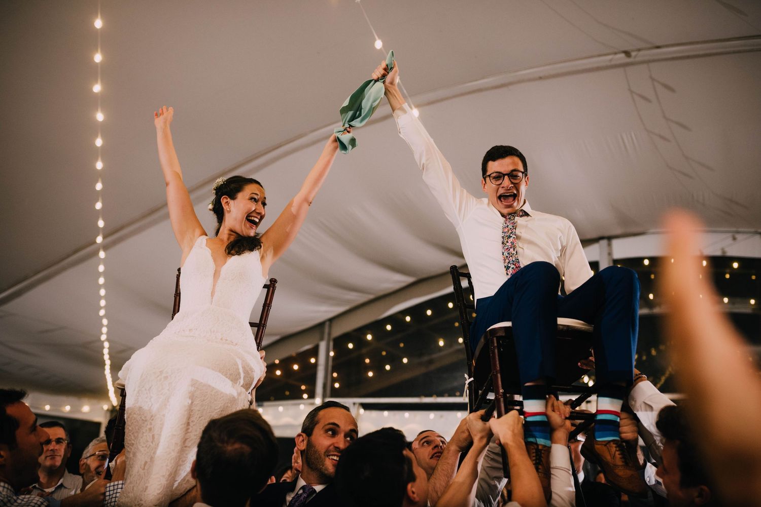 Michelle and Danny are cracking up laughing as they are thrown, on chairs, high in the air, to the Horah.