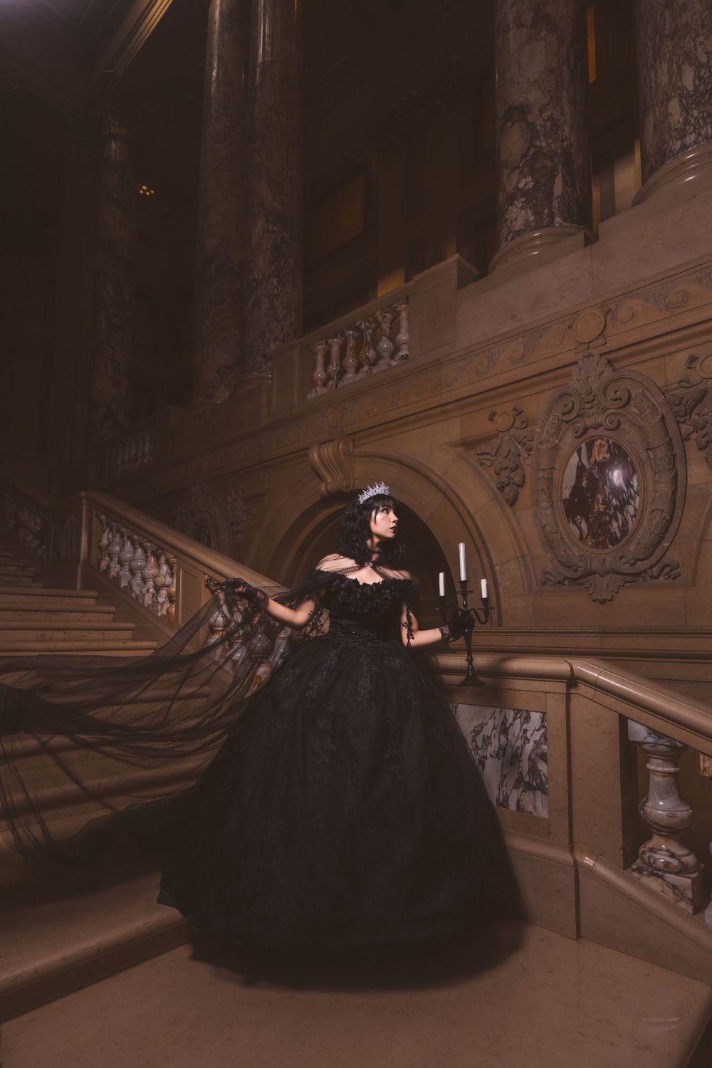 A dramatic photo of a black ball gown on an elegant staircase in a historic building.
