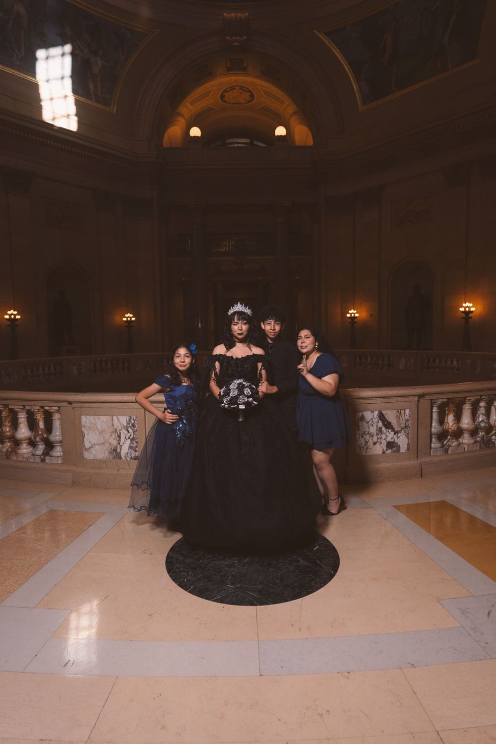 Group poses in a grand historic ballroom with decorative walls and lighting.