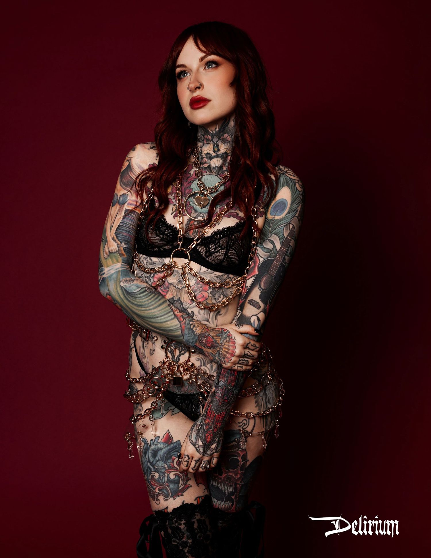 Erin an extremely tattooed model with red hair is wearing lingerie and lace boots looking at camera