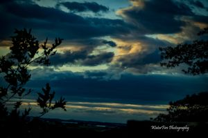 Dark stormy clouds roll across a dramatic sunset skyline over water.