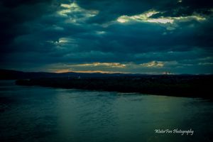 Moody seascape with dark clouds and rays of sunlight breaking through over water.