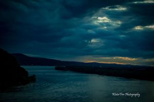 Dramatic dusk landscape with silhouetted coastline under brooding storm clouds.