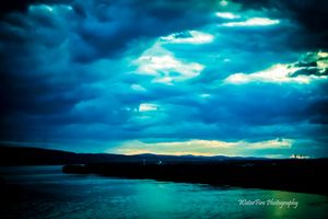 Ethereal aqua light breaks through storm clouds over a coastal waterscape.