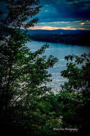 Lush green foliage frames a dramatic view of a coastal bay under stormy skies.