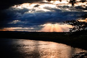 Golden sunbeams pierce through dramatic storm clouds over a tranquil ocean vista.