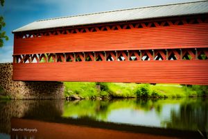 Panoramic view of a historic red covered bridge reflecting in calm waters below.
