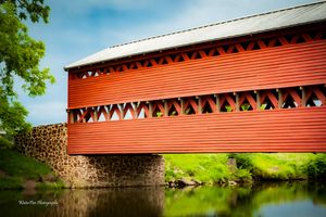 Scenic landscape of red covered bridge stretching across river under blue sky.