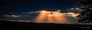 Dark clouds part to reveal dramatic sun rays shining through a stormy sky at sunset in a rural landscape.