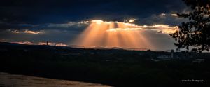 Dramatic sunbeams burst through dark storm clouds over a mountain landscape during sunset creating a dramatic natural light show.