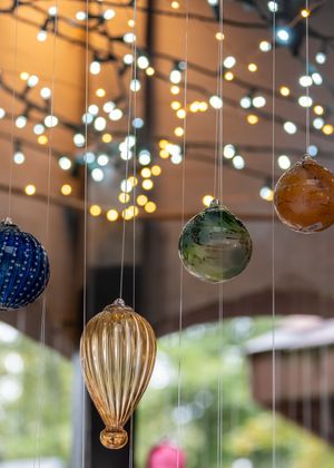 Colorful glass ornaments and string lights create a magical holiday display with bokeh effect in the background.