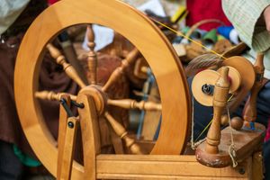 Traditional wooden spinning wheel with spools and bobbins for yarn spinning shown in close-up detail.