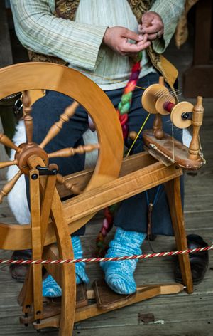 Traditional wooden spinning wheel being operated with bright blue knitted slippers visible below.
