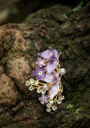 Delicate butterfly brooch with purple enamel wings, pearls, and crystal accents rests on mossy stone in natural light.