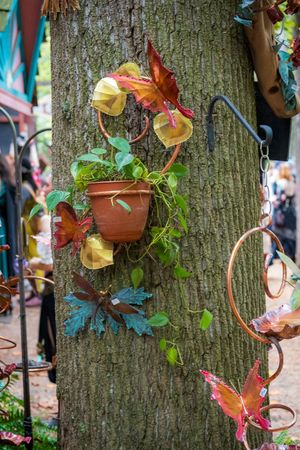 Decorative butterflies and potted plants adorn a tree trunk at an outdoor festival or market display.