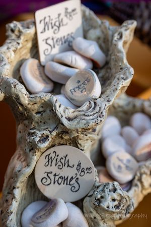 An artistic display of white ceramic wish stones with handwritten text arranged on a textured stone surface.