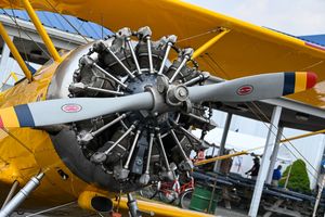 Yellow vintage aircraft with radial engine and distinctive propeller on display at an outdoor aviation event.