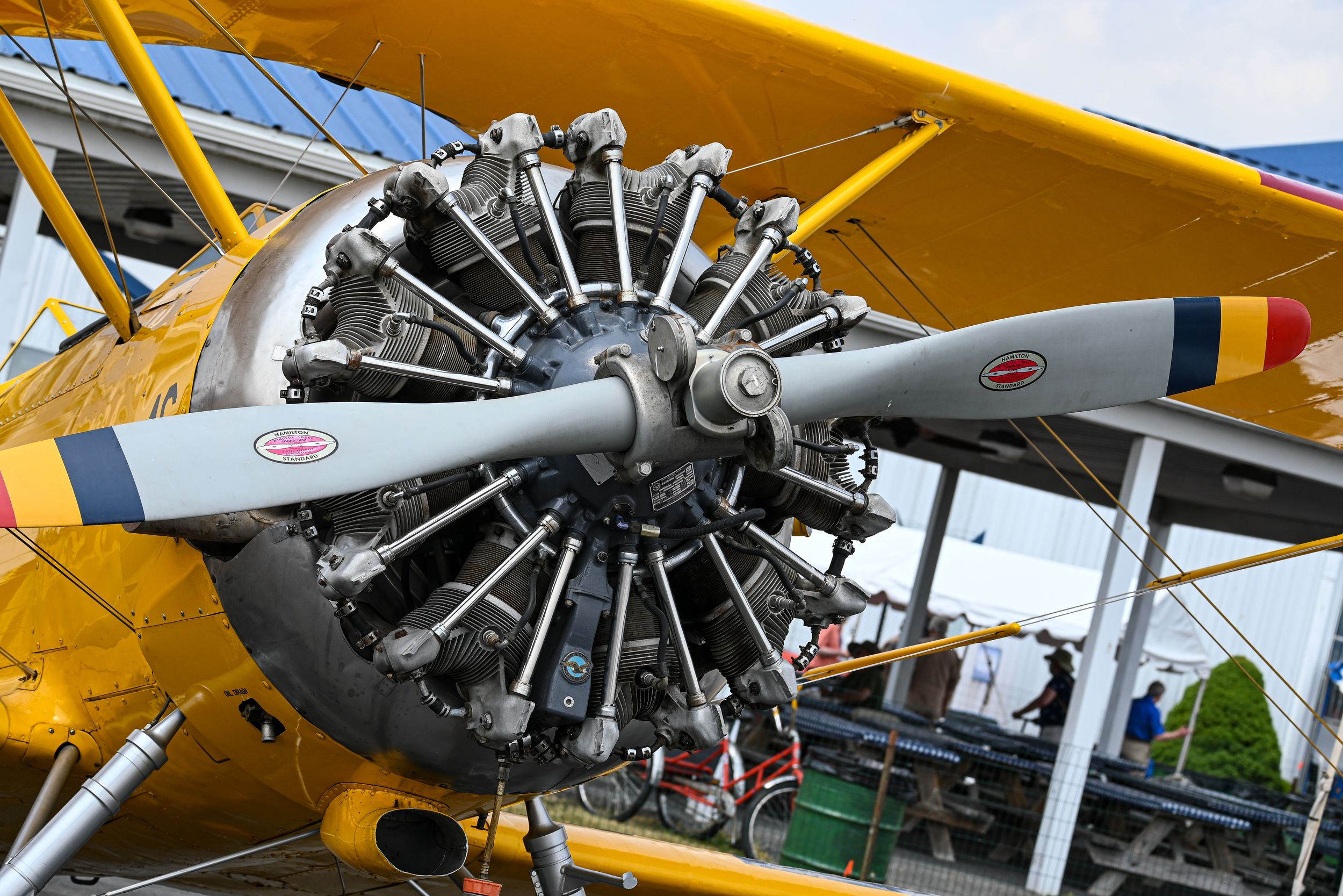 Yellow vintage aircraft with radial engine and distinctive propeller on display at an outdoor aviation event.