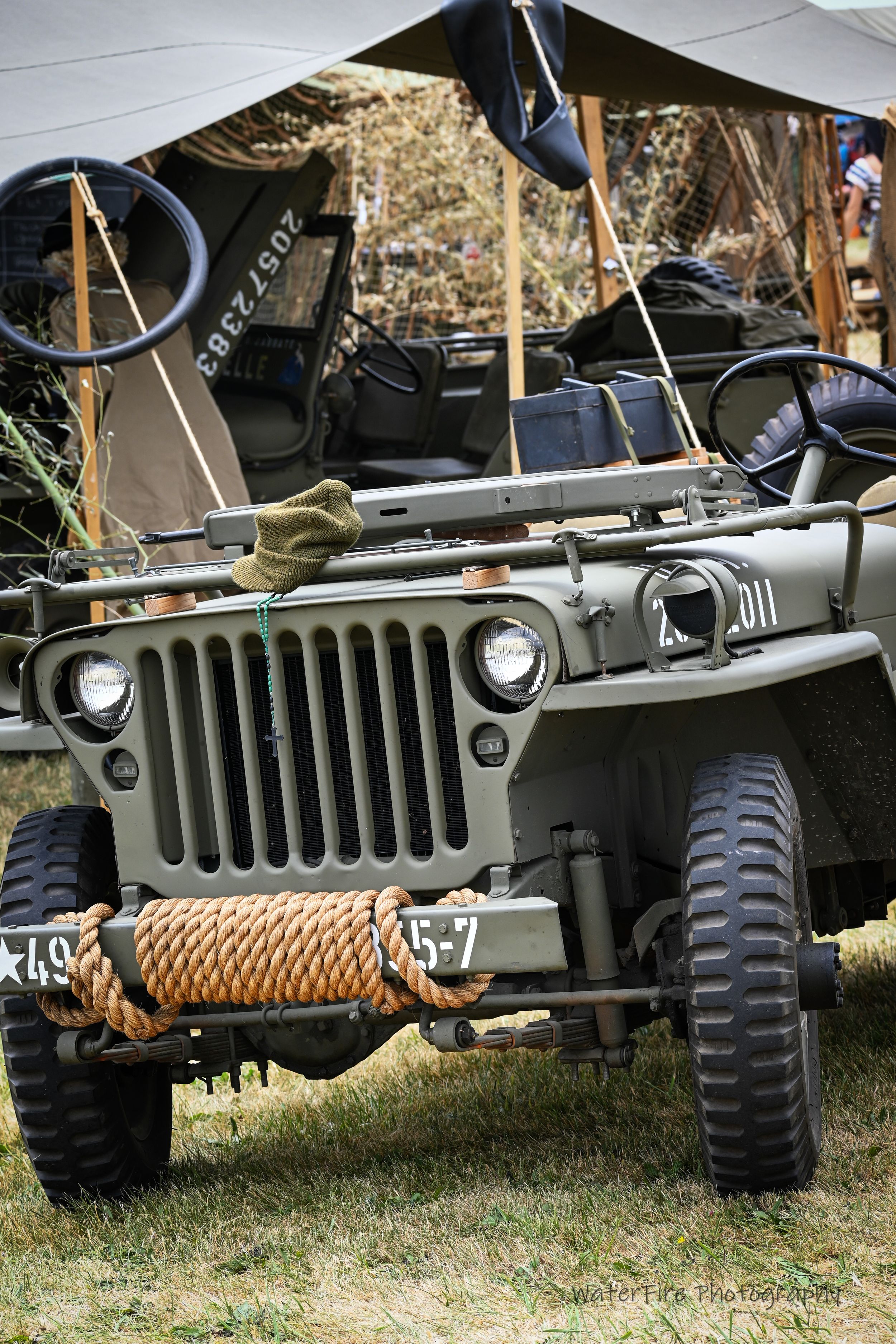 Vintage military Willys Jeep on display with rope winch and camping equipment in outdoor setting.