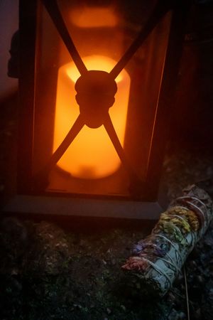 A glowing orange lantern casts warm light in darkness next to a weathered log on the ground.