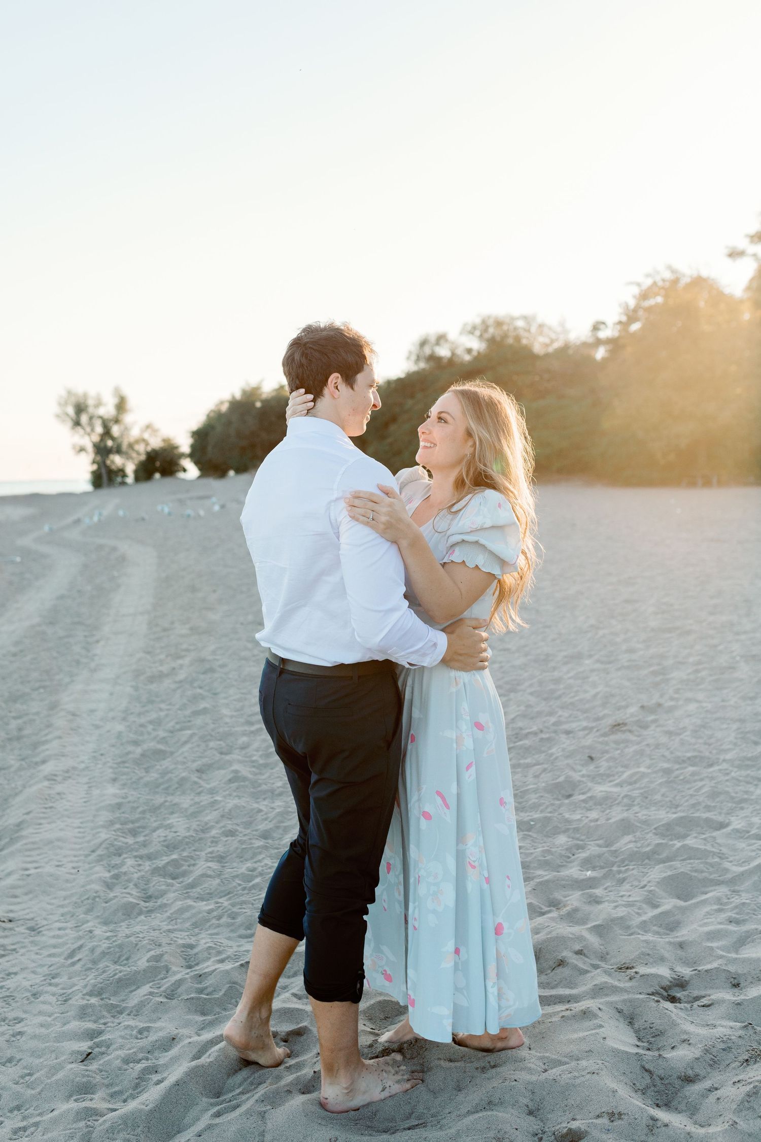 Couple embracing on sandy beach during golden sunset hour.