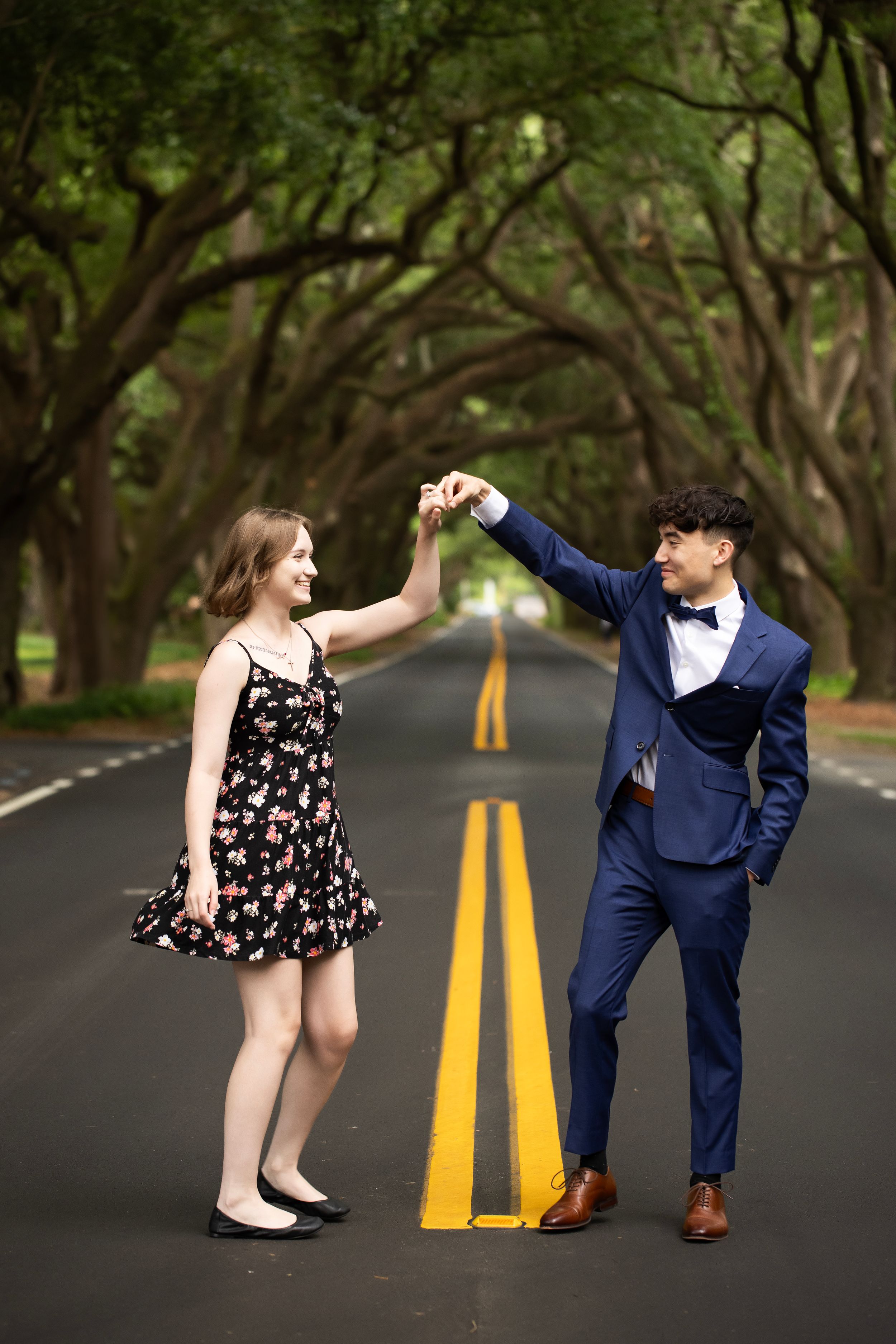 Senior boy and girl dancing in the middle of the road.  He is in a suit and she is in a floral dress.