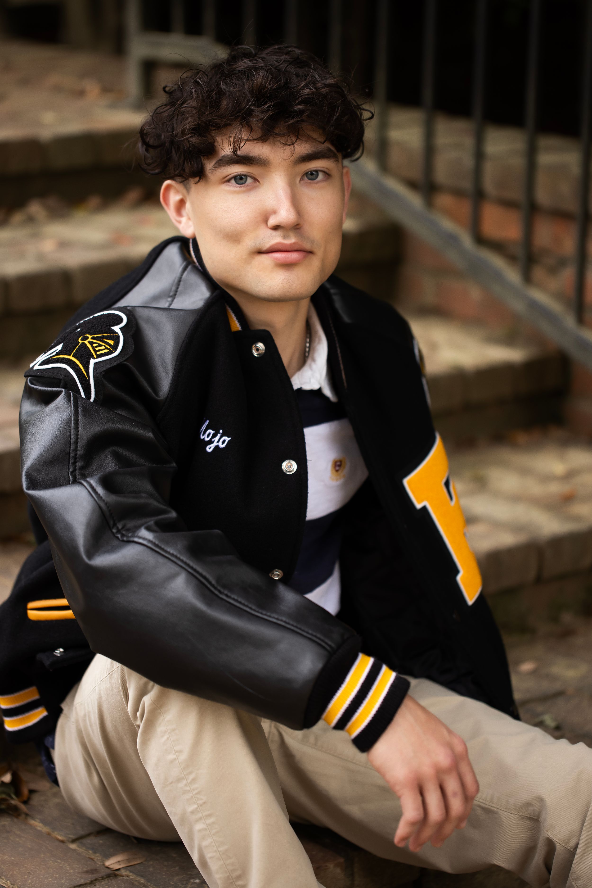 Senior boy wearing his letterman jacket and sitting on brick steps.