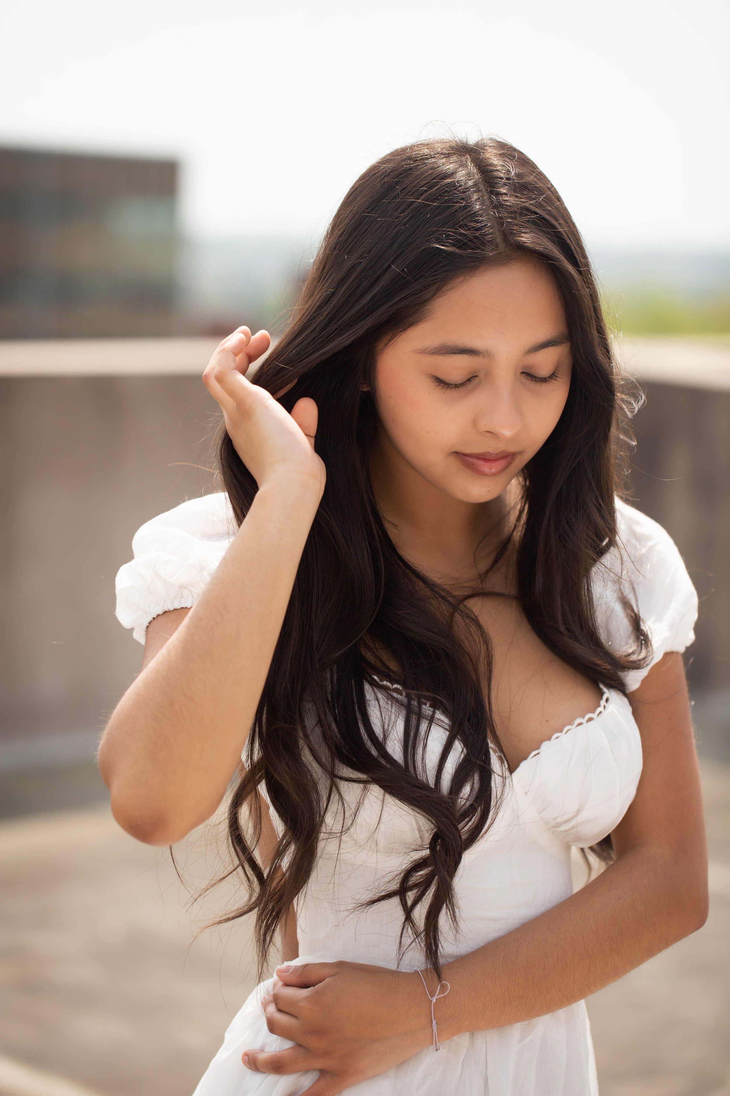 Senior girl standing on top of a parking garage wearing a white dress.