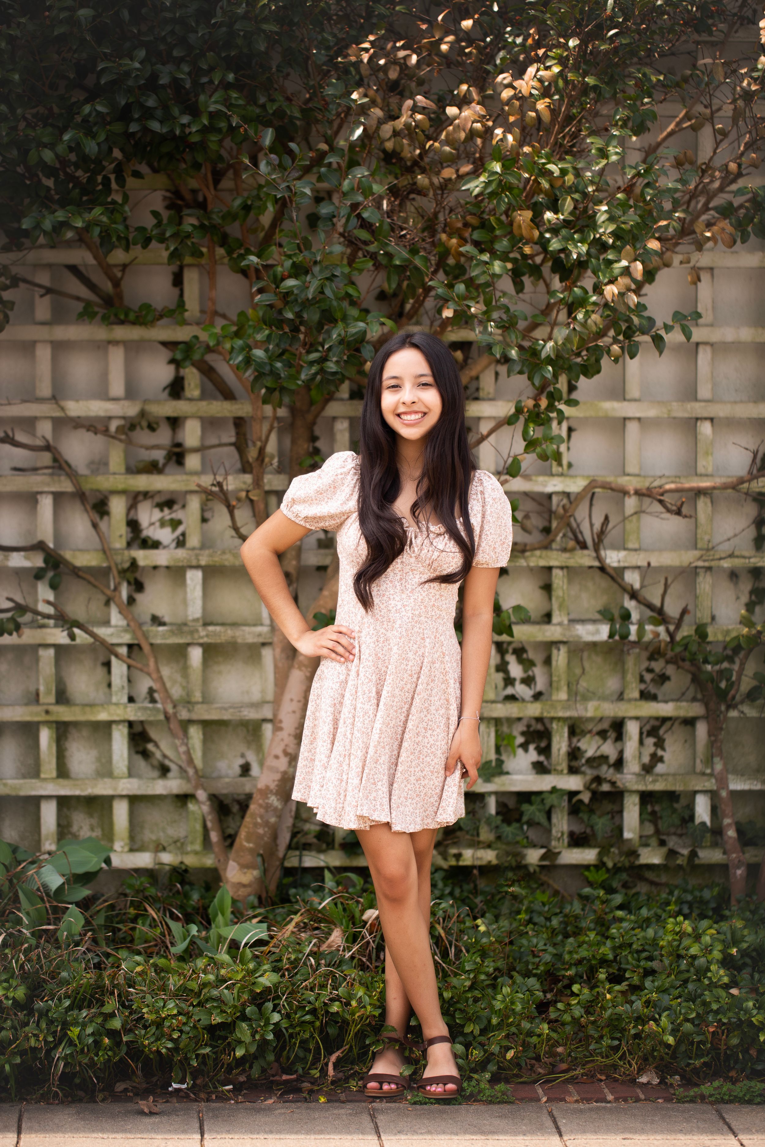 Senior girl wearing a pink dress standing in front of a lattice of vines.