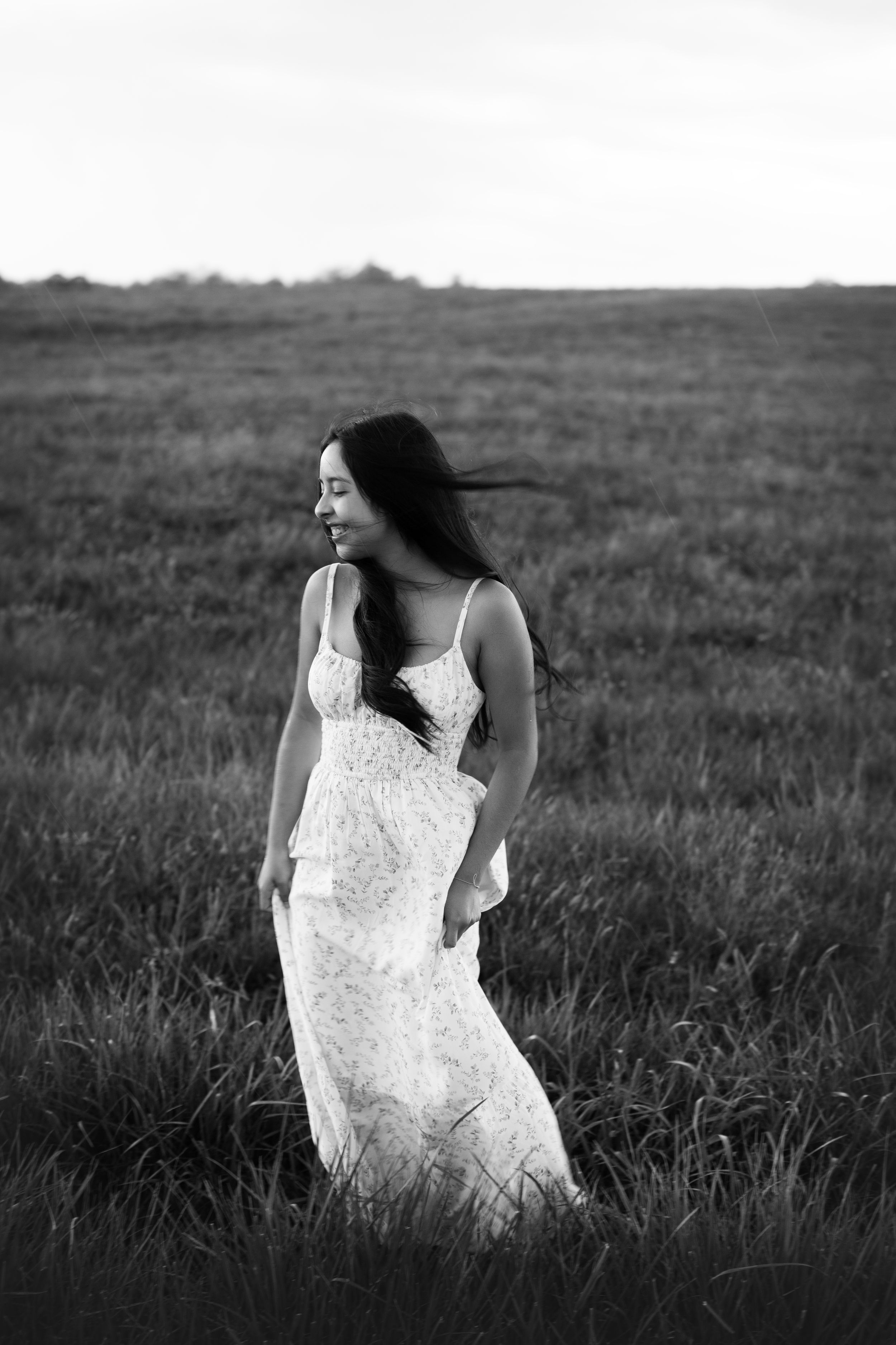 Black and white image of a girl standing in a field with the wind blowing.