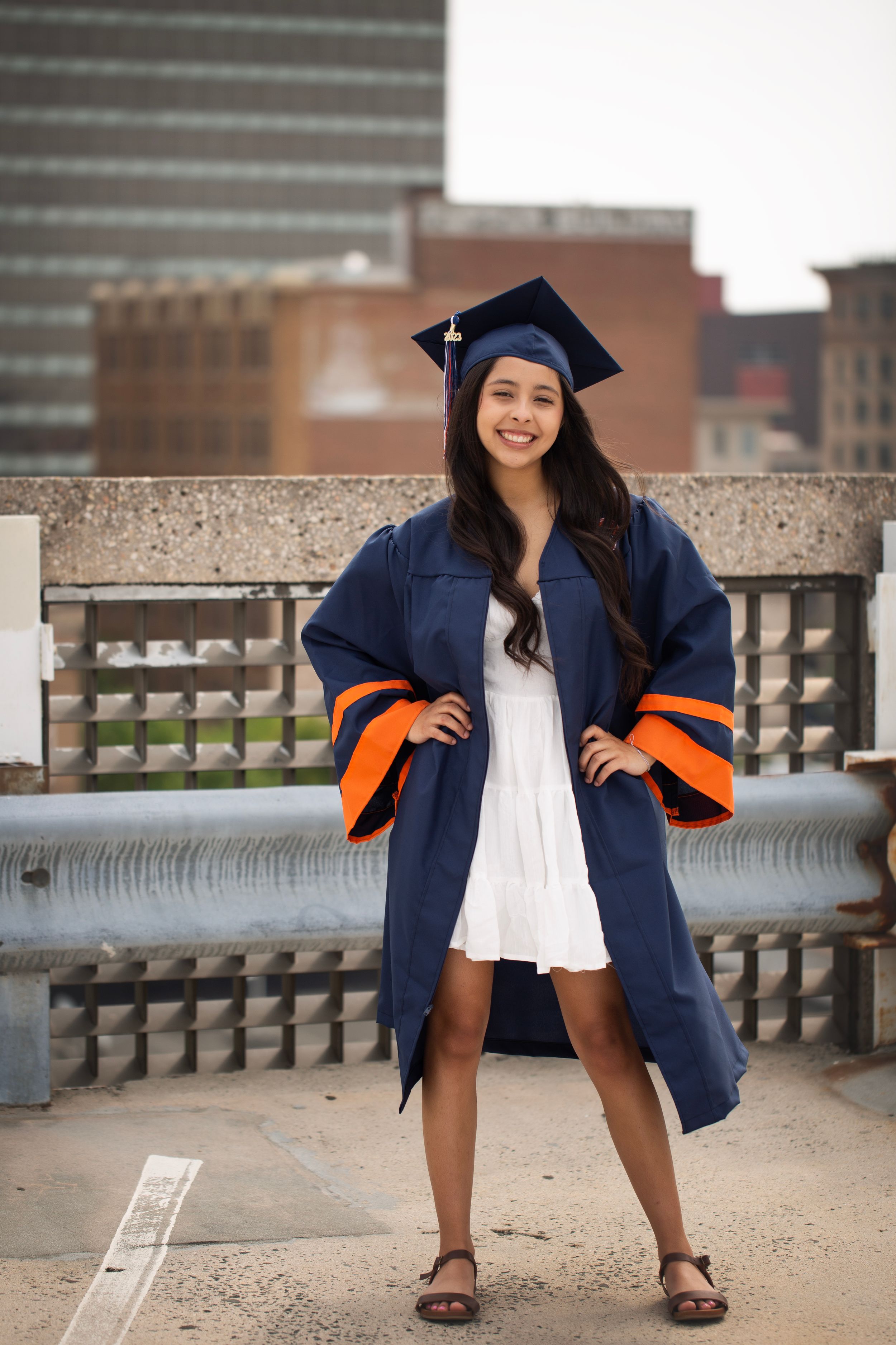 Senior girl standing on the top of a parking garage.  She is wearing her cap and gown.