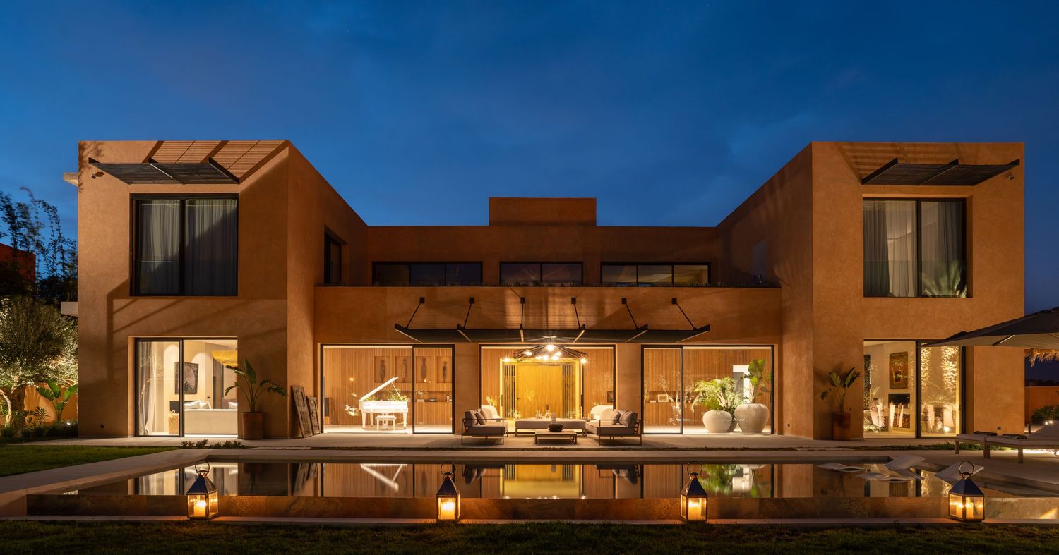 Modern Southwestern-style luxury home with warm lighting and reflective pool at twilight showcasing adobe architecture.