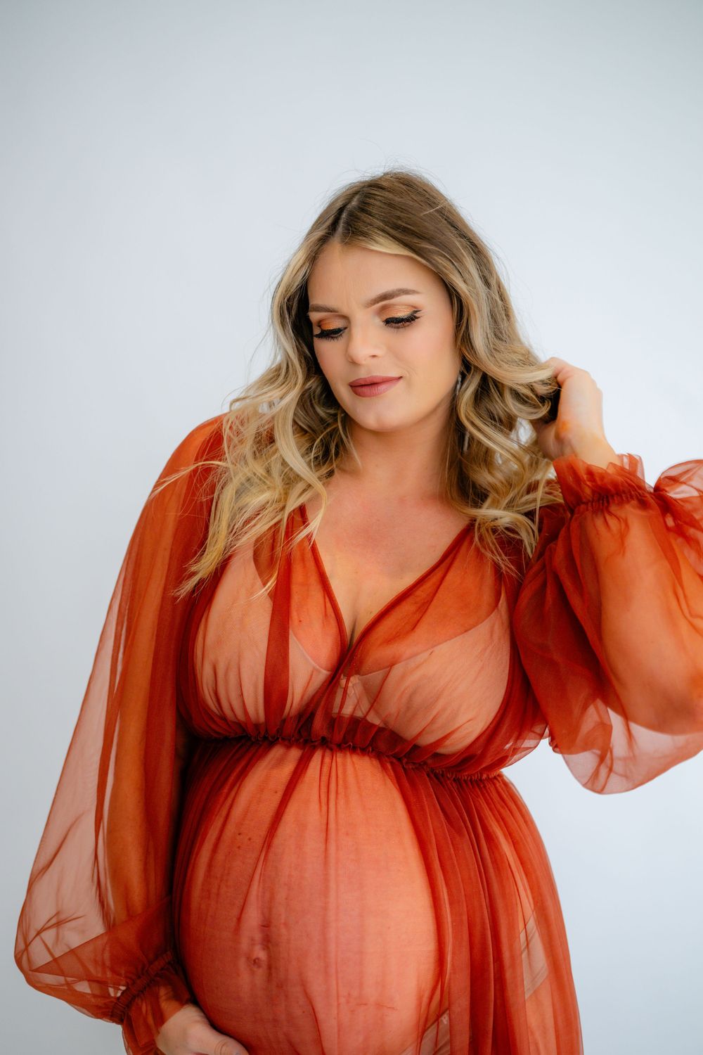 Intimate studio maternity portrait featuring soft lighting and rust-colored dress.