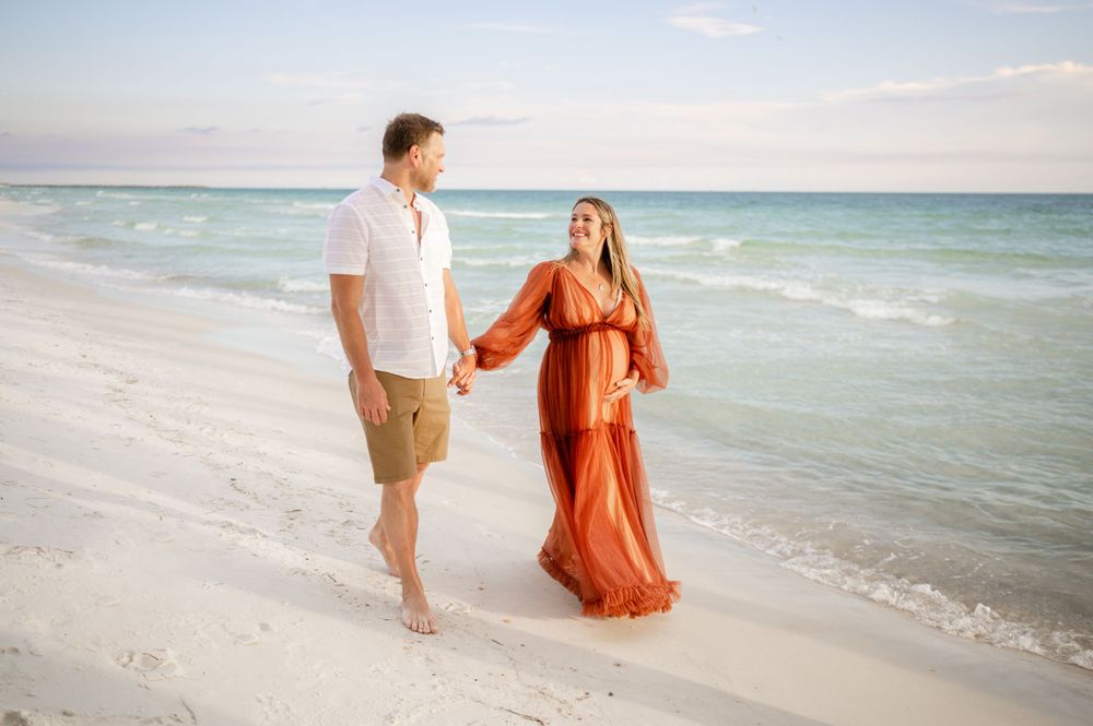 Couple walking along shoreline with turquoise ocean waves in background.