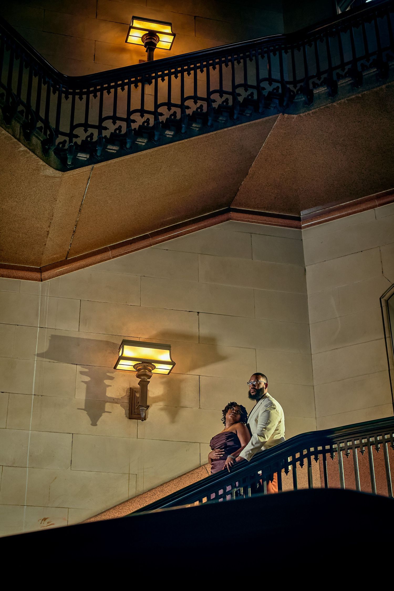 A dark architectural interior shot showing a curved staircase with ornate railings and warm lighting on the walls.