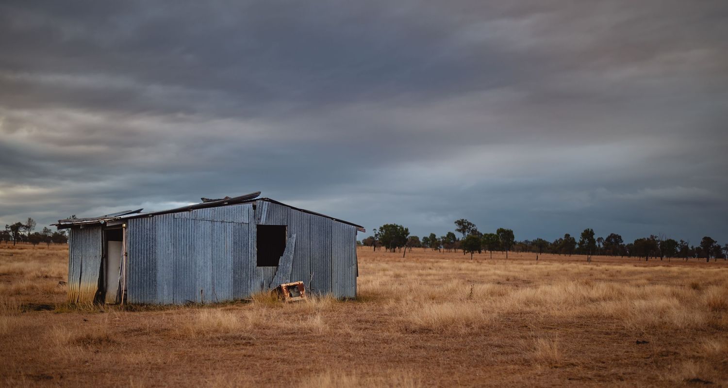 Rustic metal shed stands alone in dry grassland under cloudy sky.