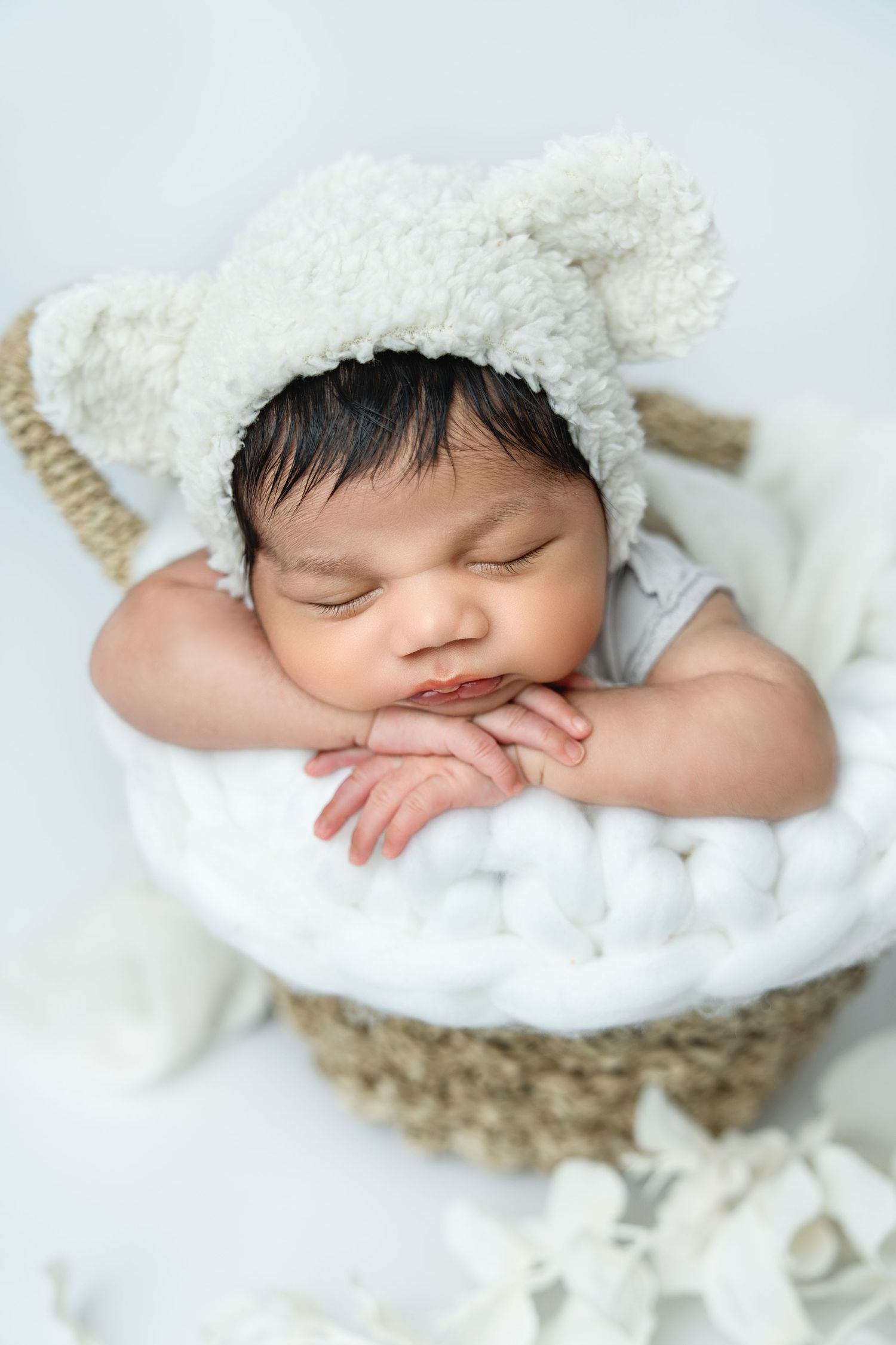 Sleeping newborn wrapped in white fuzzy blanket on soft textured backdrop.