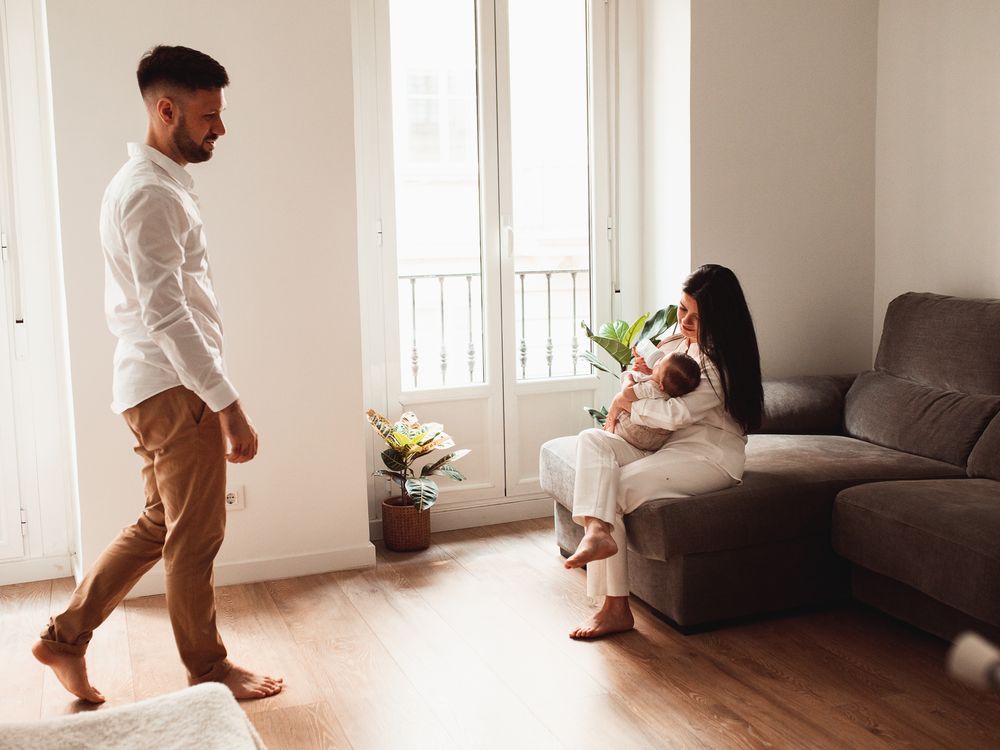 A family shares intimate bonding moments with their newborn in a sunlit room with white walls.