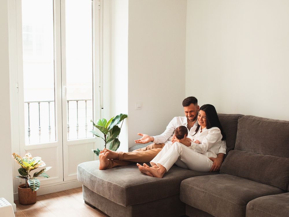 Family relaxing together on a grey couch in a modern living room with plants.