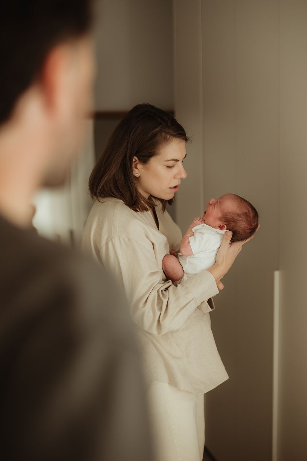 A young mother tenderly holds her newborn baby in her arms while a man stands in the foreground.