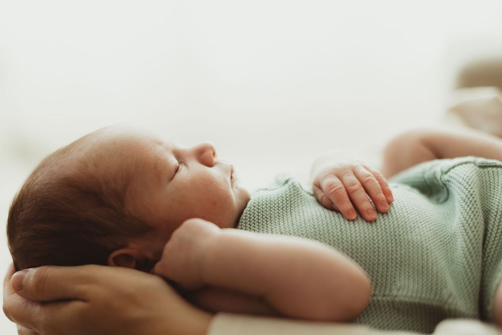 Peaceful newborn baby sleeping in a mint green onesie, with delicate features and tiny hands visible.